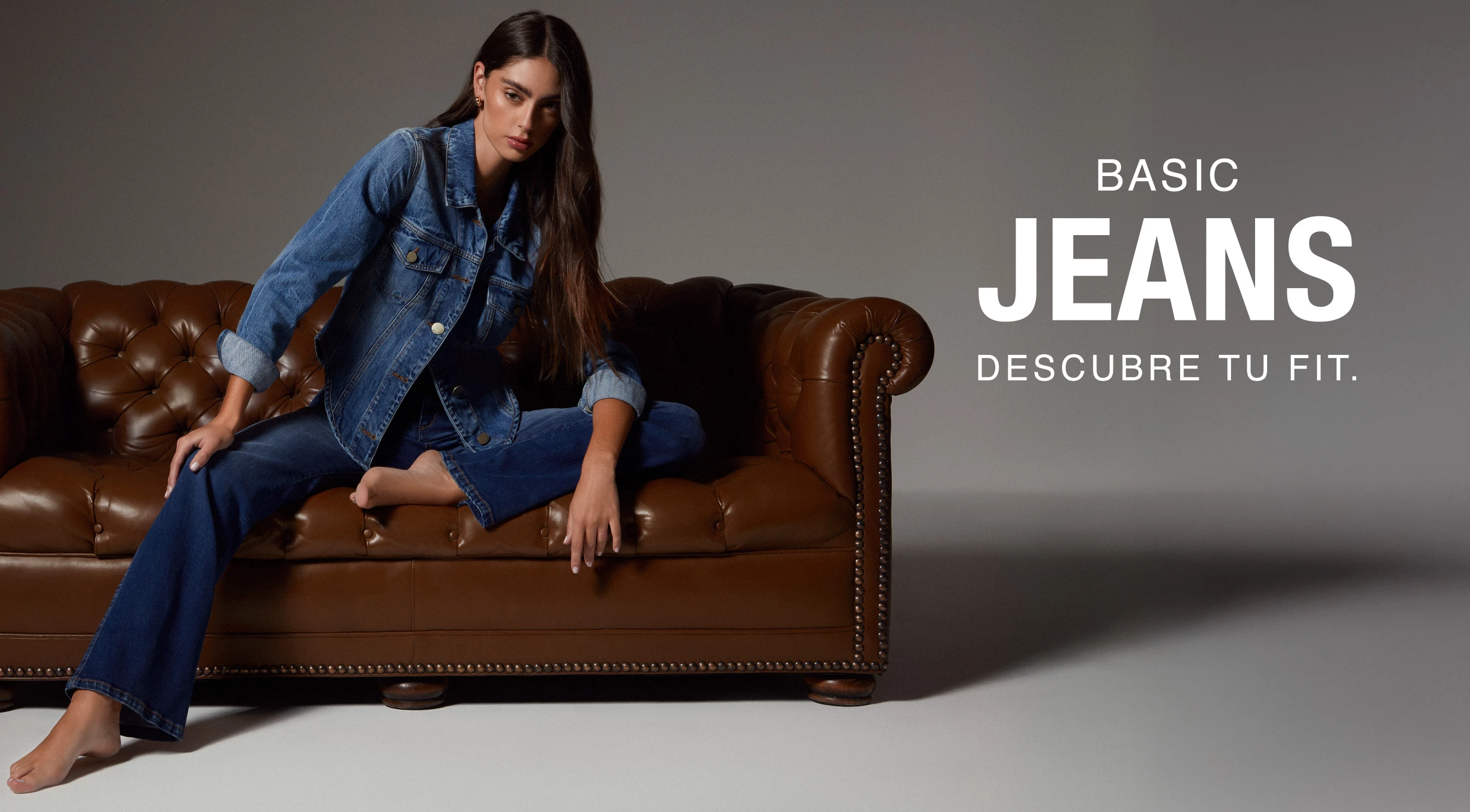 Foto de mujer luciendo look compuesto por chaqueta en denin y pantalon jean sobre sillón café​